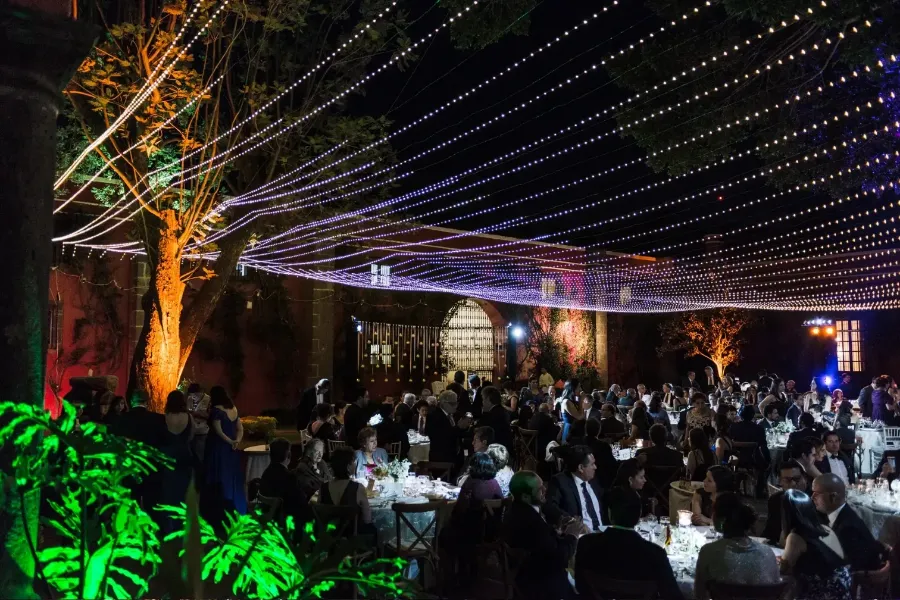 Hilos de luz tendidos entre árboles sobre las mesas de un patio